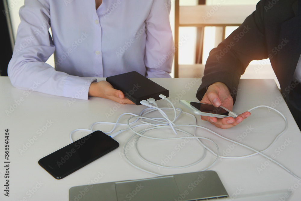 Poster two people using two mobile phone sharing usb power bank on a table to charge the mobile devices.tec