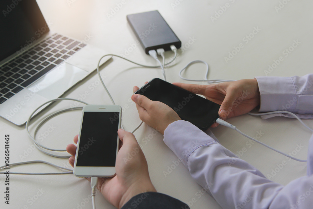 Poster two people using two mobile phone sharing usb power bank on a table to charge the mobile devices.tec