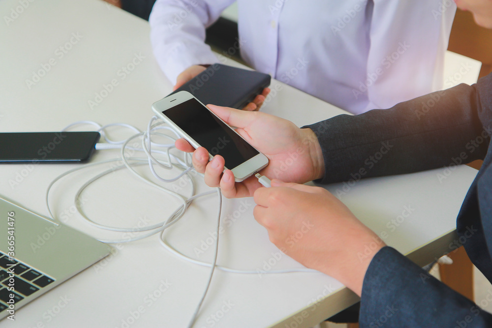 Poster two people using two mobile phone sharing usb power bank on a table to charge the mobile devices.tec