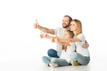 happy family sitting on floor with crossed legs and showing thumbs up isolated on white