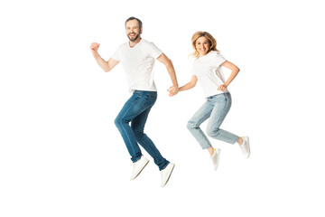 Fototapeta na wymiar happy adult couple in white t-shirts holding hands while jumping isolated on white