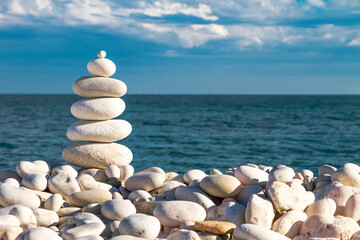 Tourette Rock Zen Pyramid of white pebble on the stones beach on a background of horizont line of blue sea and cloud sky.