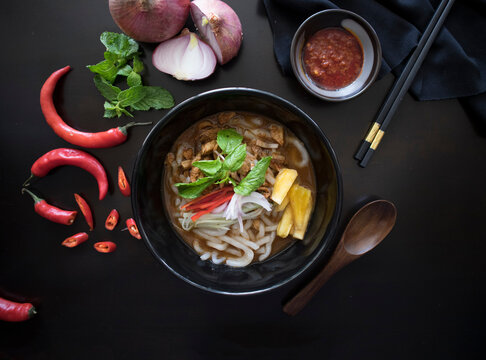 Penang Laksa Noodle Soup Flat Lay With Ingredients On A Black Table. Malaysian Assam Laksa On A Dark Wooden Table With Ingredients Spread On The Table.