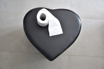 top view of a black heart and toilet paper on a gray background