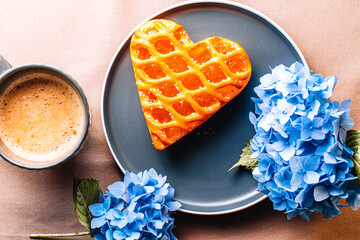 Heart shaped cookie with jam on gray plate with blue hydrangea flowers.  photo with food for bloggers. coffee is taken in the morning with sweet cakes and beautiful flowers