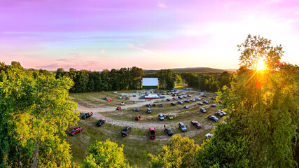 Outdoor Drive-In Movie Theater with Pink Sunset. Aerial drone view looking over cars from back of...