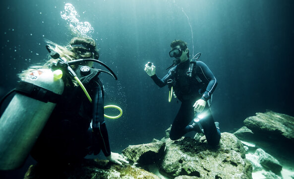Underwater view of two divers wearing wetsuits, diving goggles and oxygen cylinders.