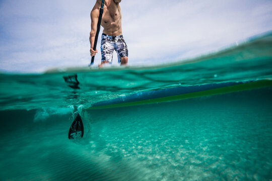 A shot of a person on a paddleboard both underwater and above the surface.