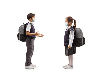 Full length profile shot of a schoolboy talking to a schoolgirl both wearing face masks