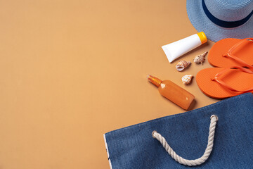Beach bag with suntan products, flip-flops and hat on beige background