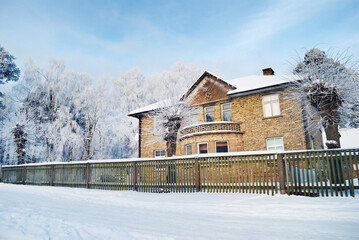 Beautiful brick house (cottage) with wooden decoration close-up. Tall trees in hoarfrost after a...