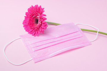 Pink protective medical face mask and flower on a pink background. Place for text.