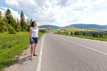 The girl on the road in the mountains catches a passing car hitchhiking