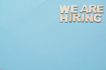 Search for employees, recruitment after crisis and coronavirus. now hiring-wooden letters on blue background. flatly with copy space, background. new hiring positions.