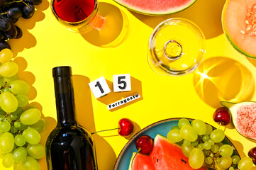 Grapes, a bottle of wine and different fruits on a yellow background. English text August 15, traditional Italian harvest day and holiday in Italy. The symbol of fun and celebration. Hard light. 