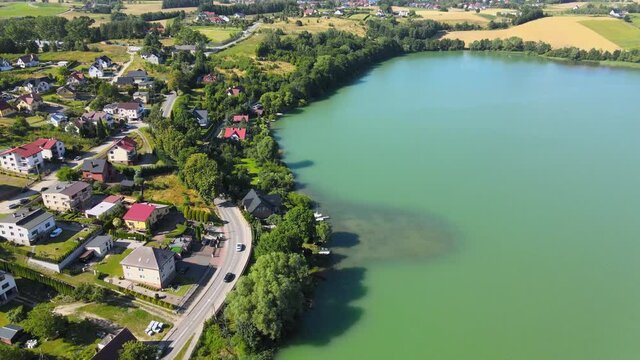 Aerial top down shot of road with cars beside lake and housing area in Chmielno,Poland