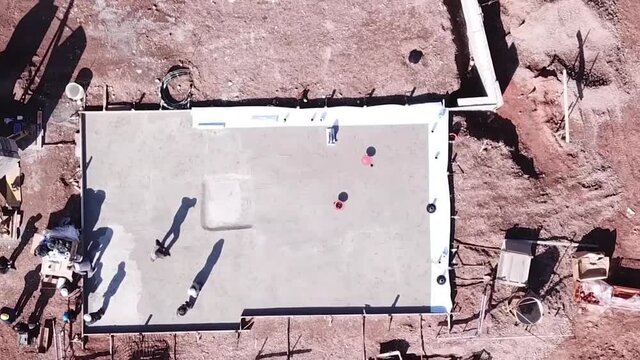 Drone descents onto a basement cement building structure in central Europe with workers being productive
