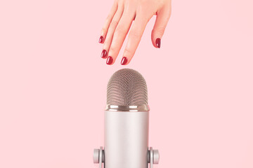 Woman hand with perfect manicure near the microphone is about to do nail tapping. Making ASMR...