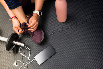 Closeup woman lacing footwear to do exercise at gym with copy space for text. Concept of healthy life and sport. Black rubber floor mat and tiles inside a gym.