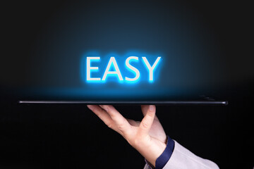 Man hand holds a tablet over which a neon text is written, the word EASY. Business concept.