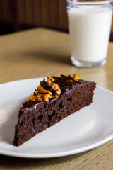 Portion of brownie cake with walnuts, glass of milk in the background