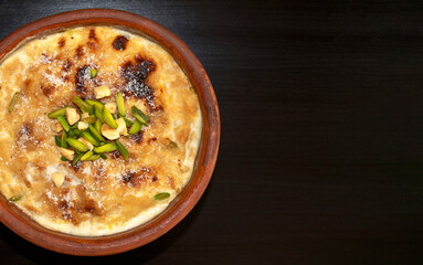 Traditional Arabic, eastern dessert Om Ali. Top view. Egyptian Bread Pudding in a brown bowl on dark wooden table with copy space. Top view. Egypt sweet pastry dessert