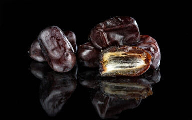 A few dried dates, a whole, and a slice on a dark mirror background..