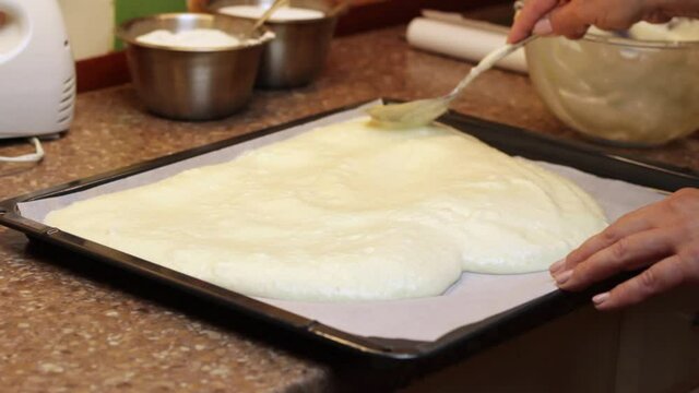 Smoothing sponge cake batter out over a cake tray with a spoon over greaseproof paper