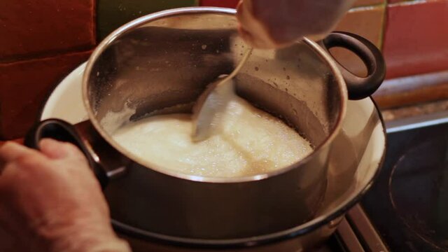 Looking down at a boiled milk icing in a saucepan in a bain marie, stirred with a metal spoon