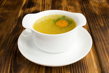 Chicken broth in the white bowl on the brown wooden background. Closeup.