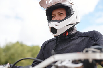 Determined motorcyclist in white helmet and jacket sitting on motorbike and looking into distance outdoors