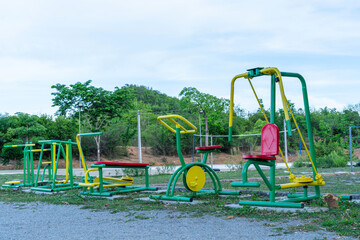 The green outdoor exercise equipment of the village are made of steel And there is a sports area in the back