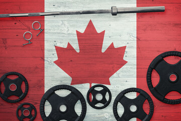 Canada gym concept. Top view of heavy weight plates with iron bar on national background.