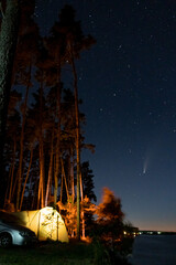 Tourist hikers tent near the lake at night with stars and Neowise comet with light tail in dark...
