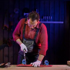 middle-aged man in jumpsuit fixing red plastic kids skateboard in carpentry. capable and reliable domestic master