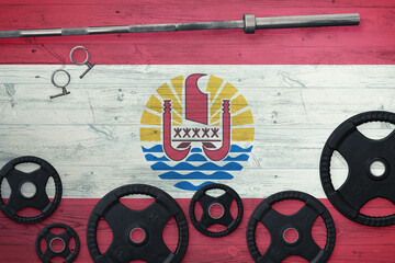 French Polynesia gym concept. Top view of heavy weight plates with iron bar on national background.
