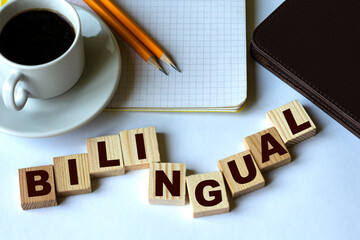 Plakat BILINGUAL word on cubes on the background of a notebook with pencils and a cup of coffee