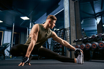 Bodybuilder stretching on floor in gym.