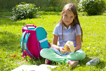 Schoolgirl in the park on the grass eating a banana
