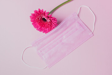 Pink protective medical face mask and flower on a pink background. Place for text.
