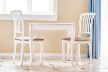 Two white chairs and white empty table by the window in a clean large room