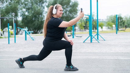 A beautiful fat girl in headphones is engaged in fitness on the sports ground and takes a selfie....