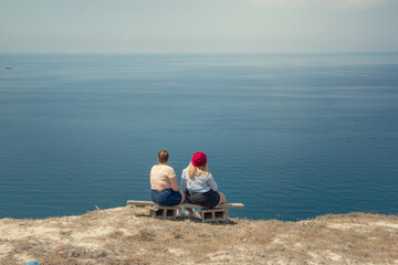 Two friends are sitting on a bench. On the edge of a cliff against the background of an amazing sea...