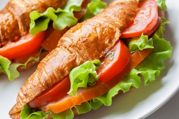 Croissant sandwich with smoked salmon, red tomato and green salad close-up, healthy breakfast, fish food