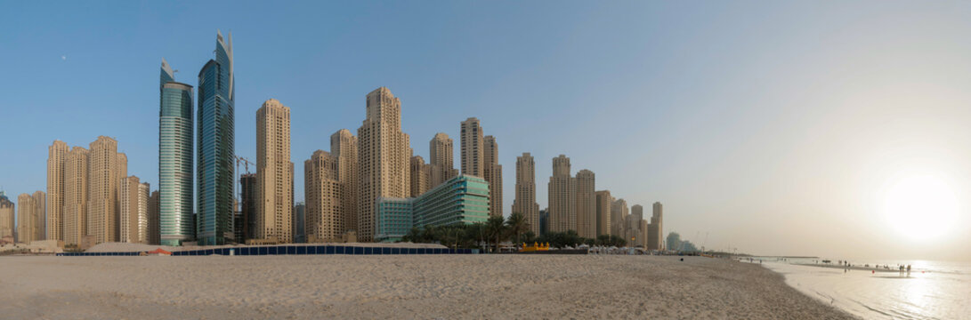 Apartment Complexes On The Dubai Shoreline. Panorama With Clear Blue Skies And Beach In The Foreground