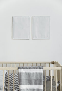 Two white empty wall frames above infant baby cot bed with gray blanket
