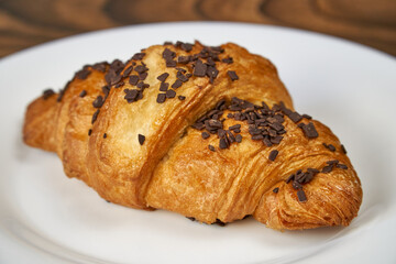 Croissant with chocolate sprinkles lies on a white plate. Close-up