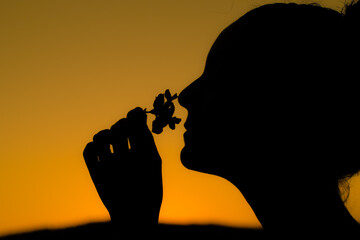 silhouette of a girl with her hair up, smelling a flower on an orange background