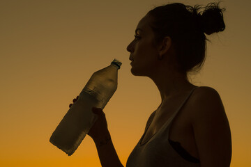 young girl drinking mineral water from a bottle with a sunset in the background