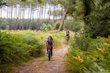 Obraz premium cute little girl riding a bicycle in the forest with her mom
